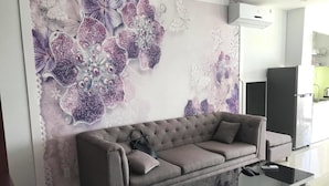 Una sala de estar moderna con un sofá gris, una mesa de centro de vidrio y un mural decorativo.