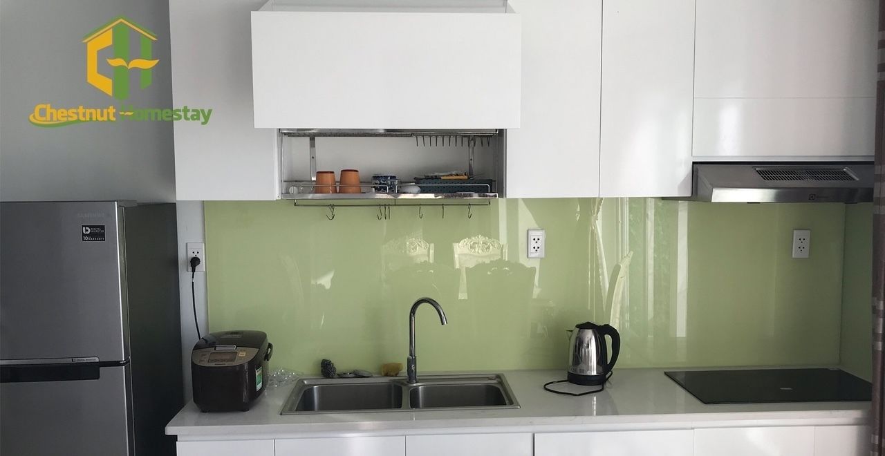 A modern kitchen with a stainless steel refrigerator, a built-in oven, a sink with a faucet, and a kettle on the countertop.