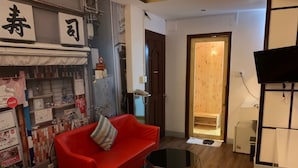 A hotel room with a red sofa, a small round table, and a bed with a red and white bedspread. There is a wooden door leading to a bathroom, and a wall with various items and a Coca-Cola sign. - Quynh Huong Hotel (Ho Chi Minh City)