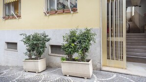 A building with two large planters on the ground floor, a staircase to the right, and a window with a yellow awning.