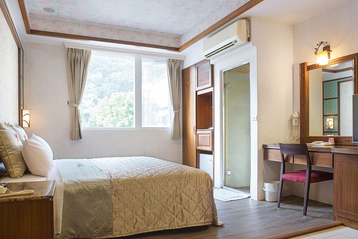 A hotel room with a bed, desk, chair, and a large window with curtains.