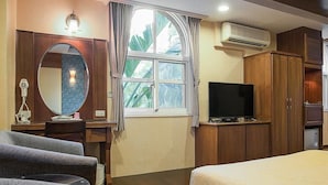 Habitación de hotel con cama, televisión, escritorio con silla, espejo y ventana con cortinas.