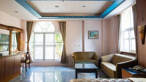 Una habitación de hotel con un ventanal grande, un sofá, una silla, una mesita y un televisor.