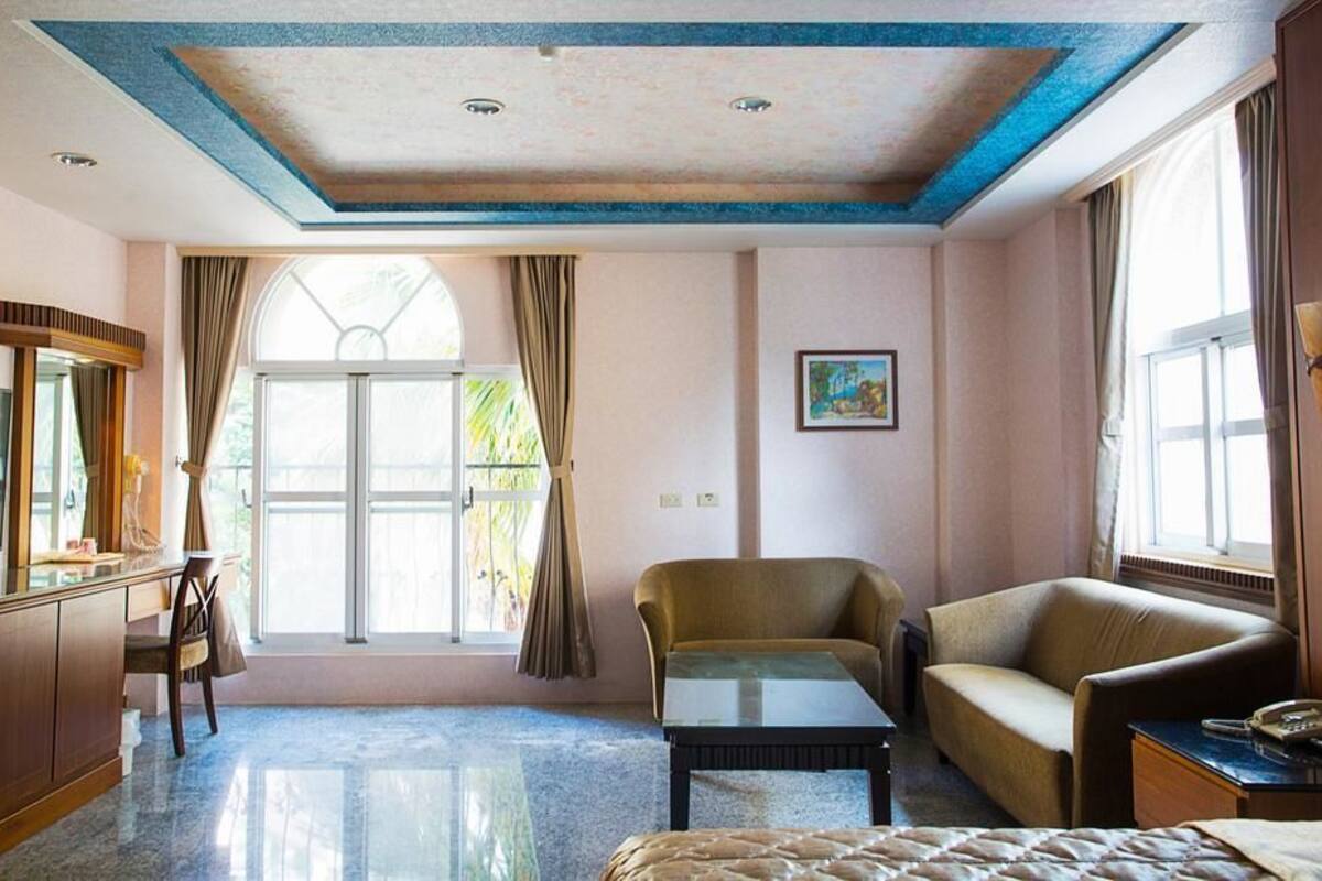 A hotel room with a large window, a sofa, a chair, a small table, and a TV.