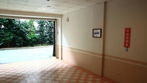 Un pasillo con suelo a cuadros, una puerta que da al exterior y un cartel rojo en la pared.