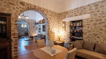 A cozy living room with a stone wall, a round wooden table, a sofa, and a bookshelf.