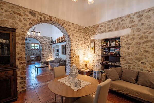 A cozy living room with a stone wall, a round wooden table, a sofa, and a bookshelf.