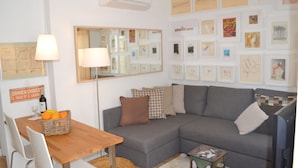 A living room with a grey sofa, a wooden dining table, and a wall decorated with framed artwork. - RH FACTORY 15, Lisbon Apartment (Lisboa)
