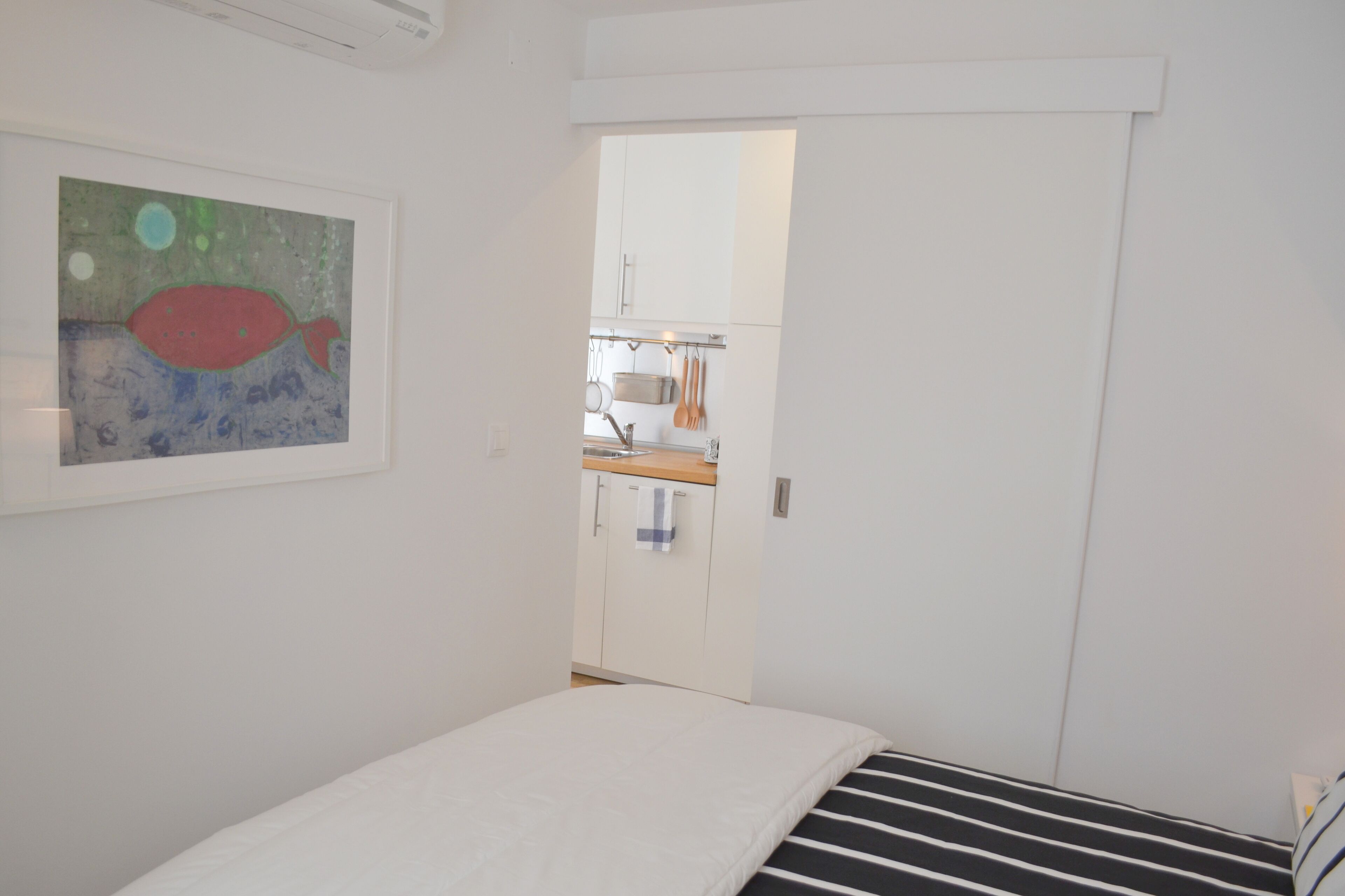 Un dormitorio con cama, un cuadro y vistas hacia una zona de cocina.