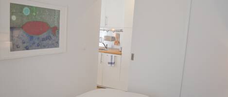 Un dormitorio con cama, un cuadro y vistas hacia una zona de cocina.