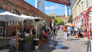A cobblestone street with outdoor seating and market stalls, under a bridge. - RH FACTORY 15, Lisbon Apartment (Lisboa)