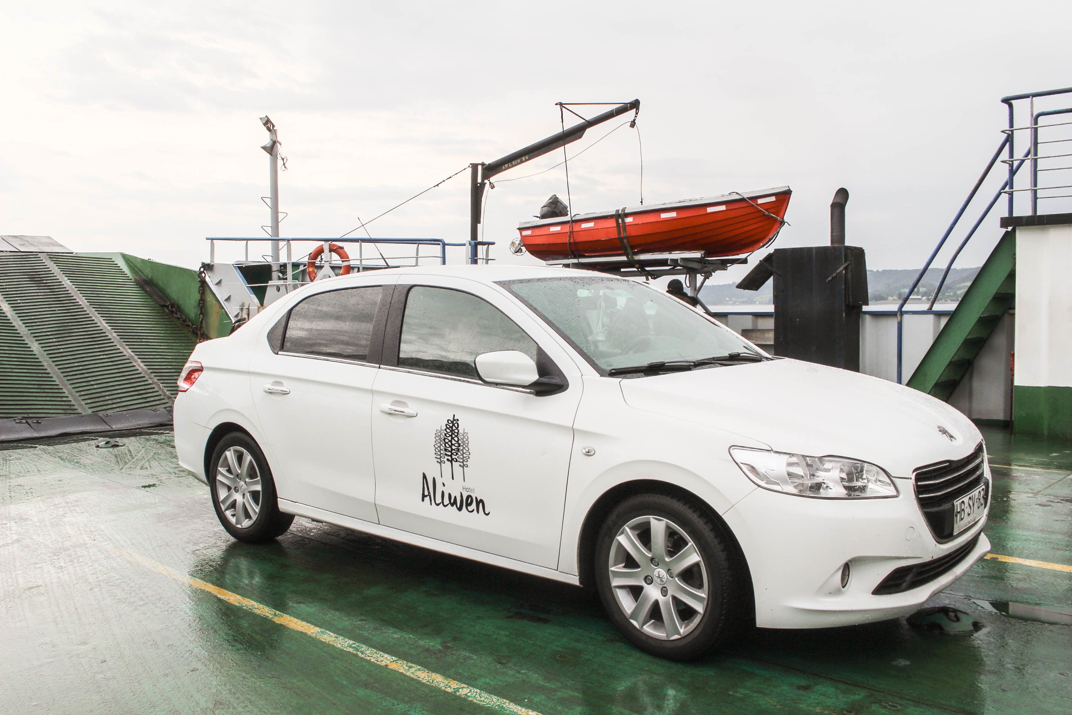 Um carro branco com a marcação 'Aliwen' estacionado em uma superfície molhada, possivelmente um cais ou navio.
