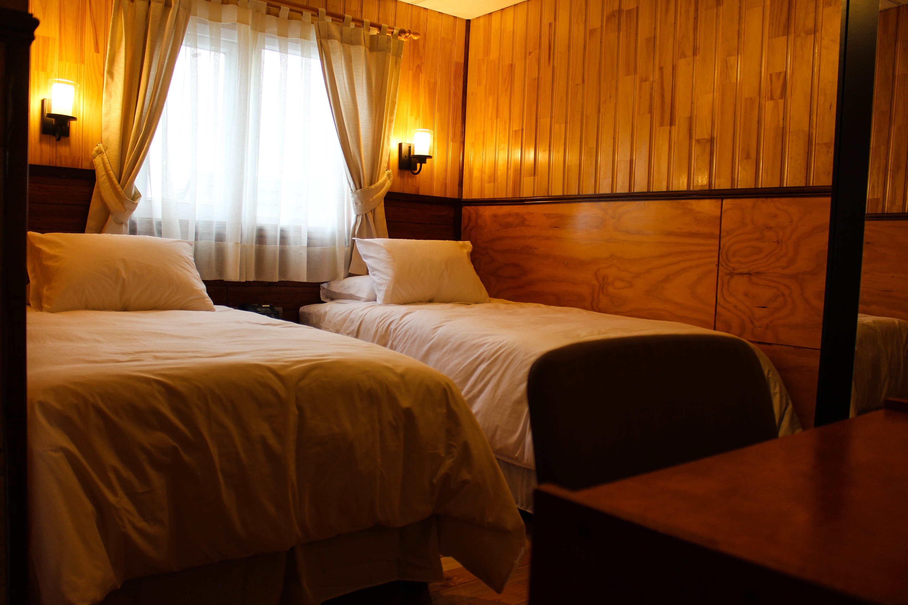 A room with two beds, wooden paneling, and two wall-mounted lights.