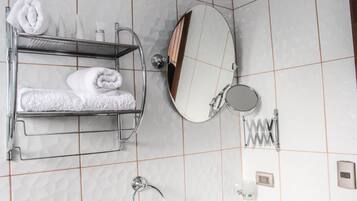 Un baño con un perchero que sostiene dos toallas dobladas con cuidado, un espejo redondo, un espejo de mano y un dispensador de jabón en la pared.