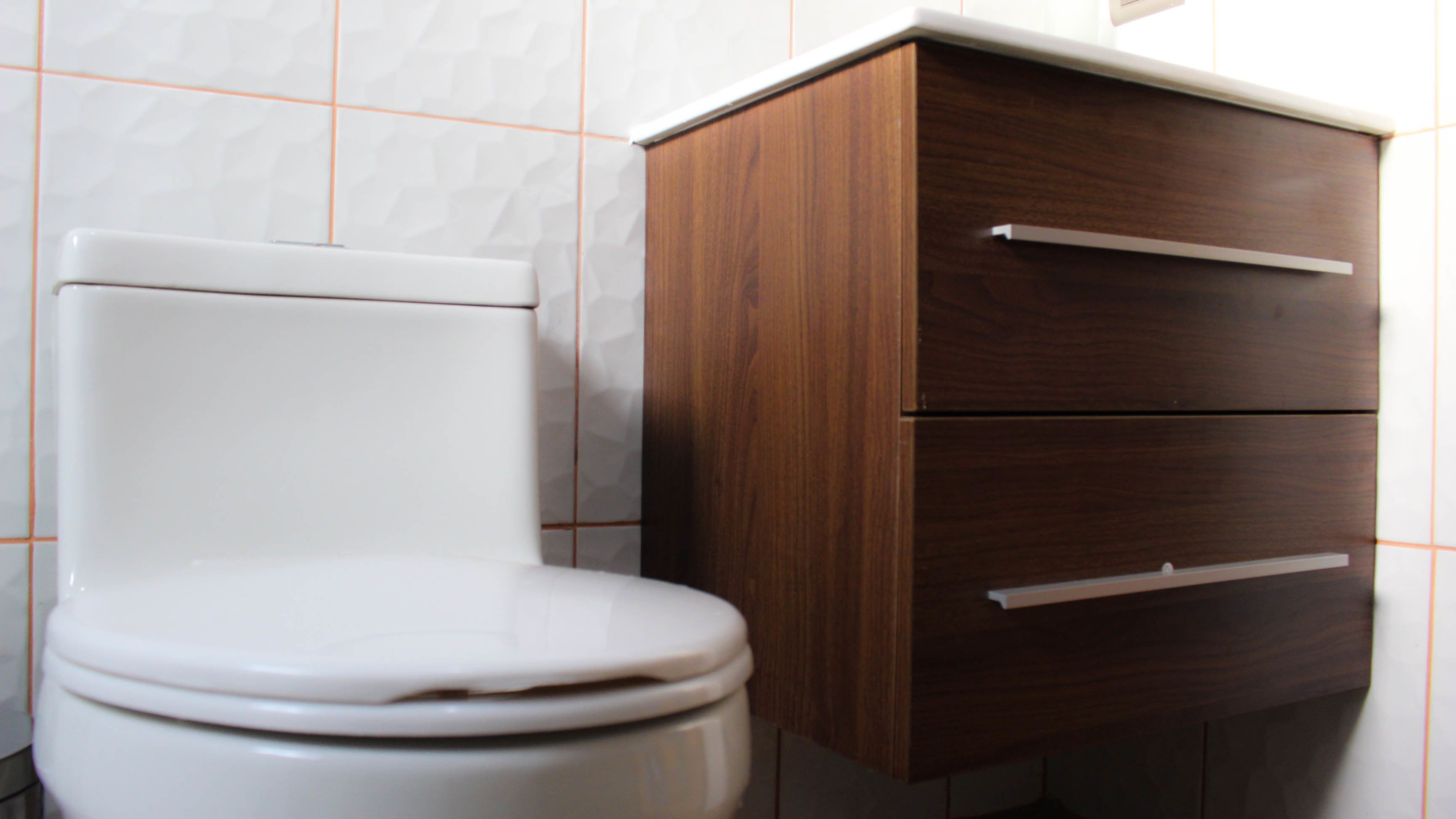 Un inodoro blanco junto a un mueble de madera con dos cajones.