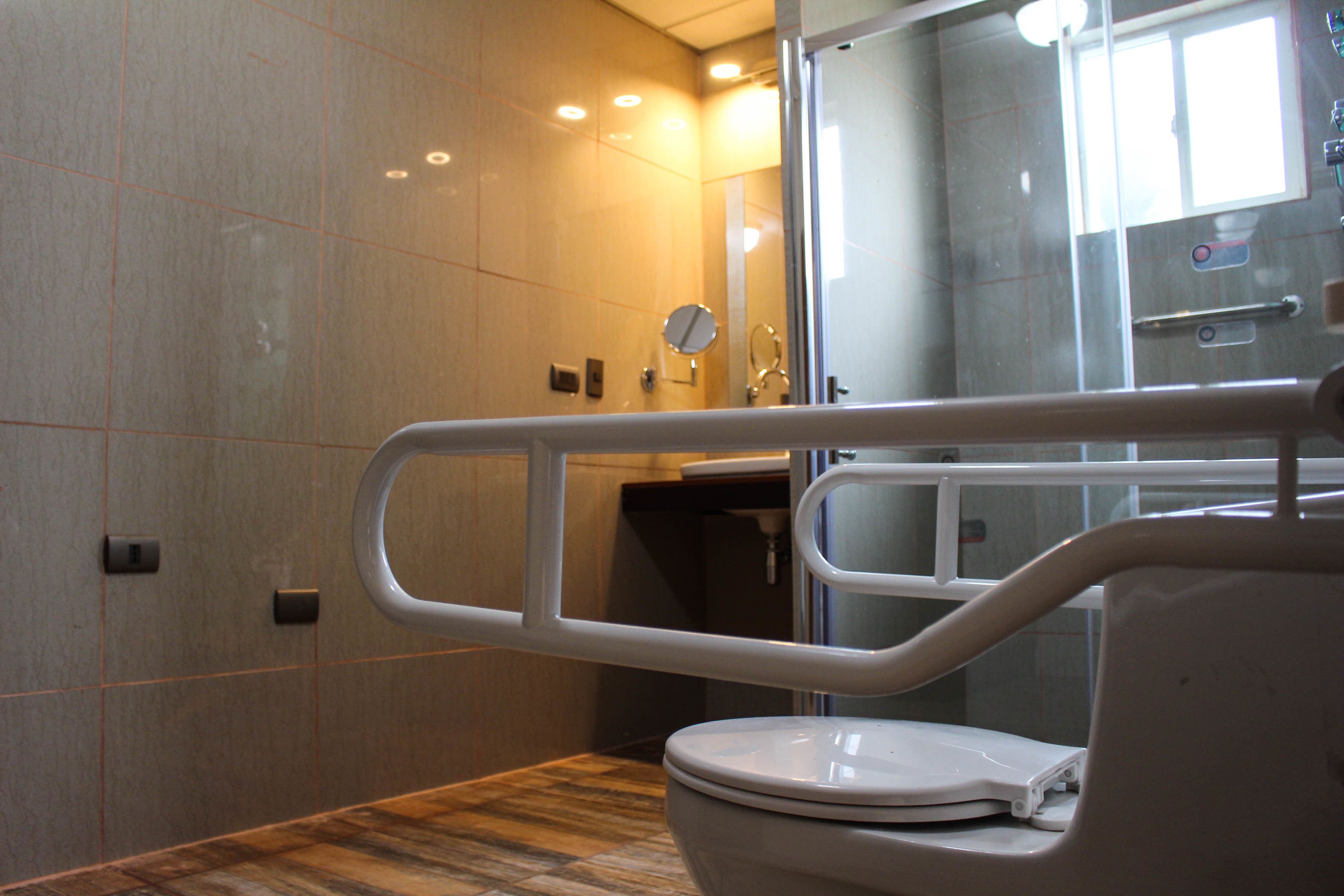 Un baño moderno con inodoro, cabina de ducha de vidrio y barra de apoyo.