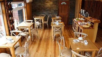 Un restaurante acogedor con mesas y sillas de madera, una pared de piedra y una barra de desayuno con diferentes platos.