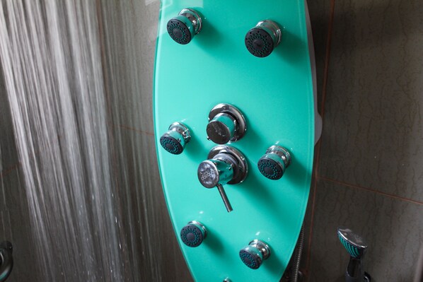 A bathroom with a turquoise showerhead and multiple knobs.
