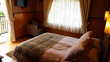 A bedroom with a bed, a chair, a television mounted on the wall, and a window with curtains.