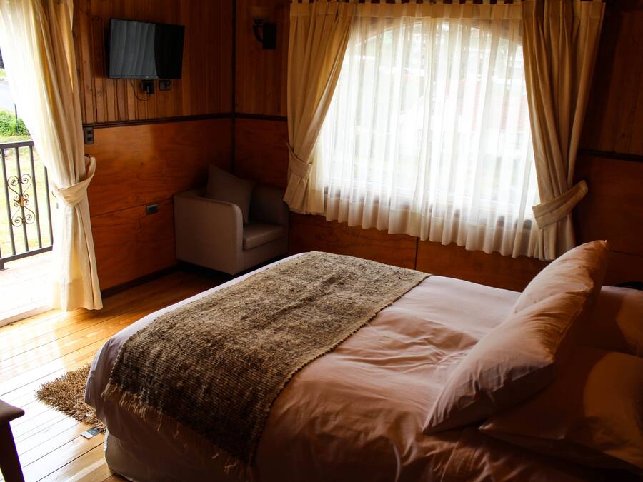 A bedroom with a bed, a chair, a television mounted on the wall, and a window with curtains.