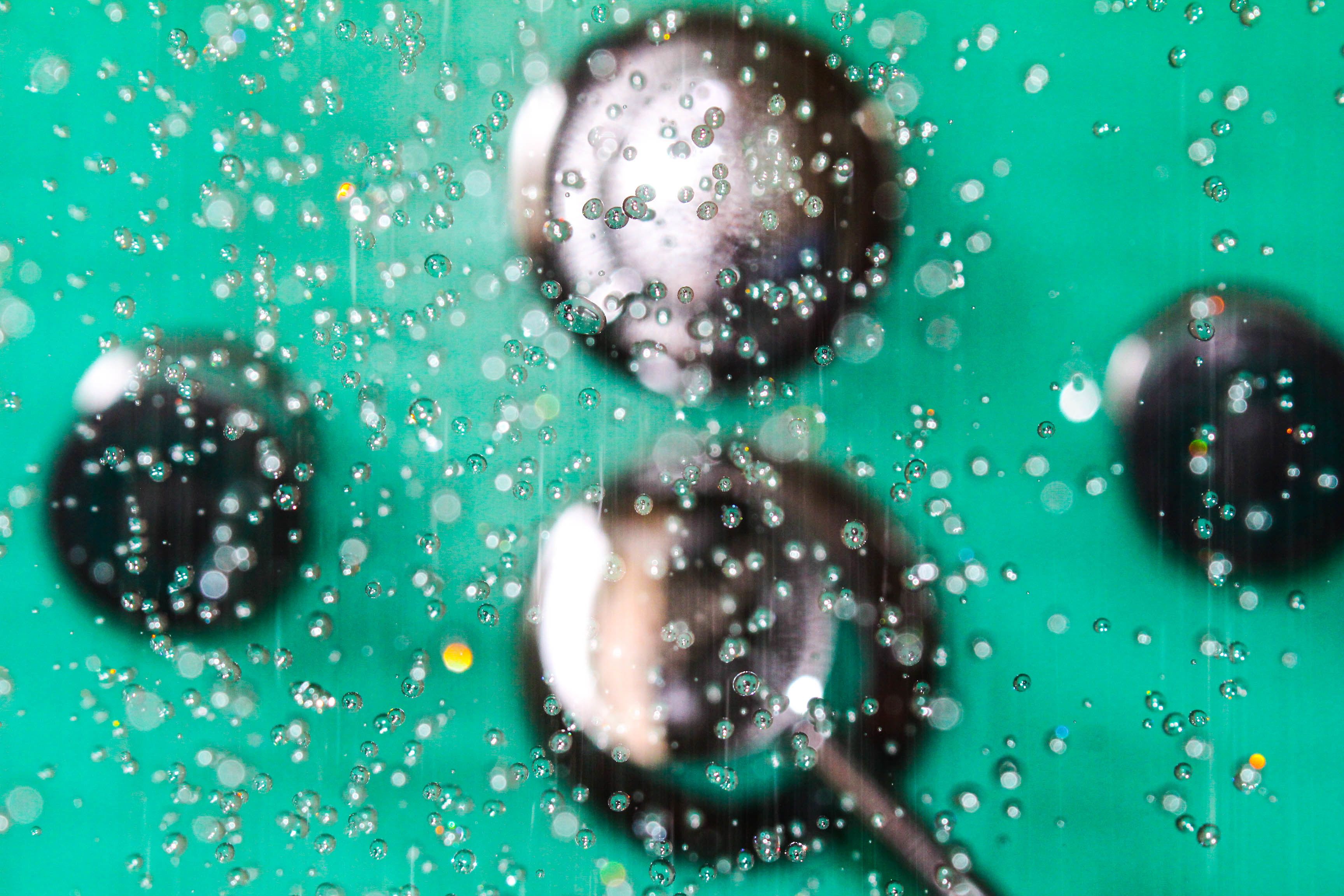 A close-up of a metallic object with water droplets on a green background.