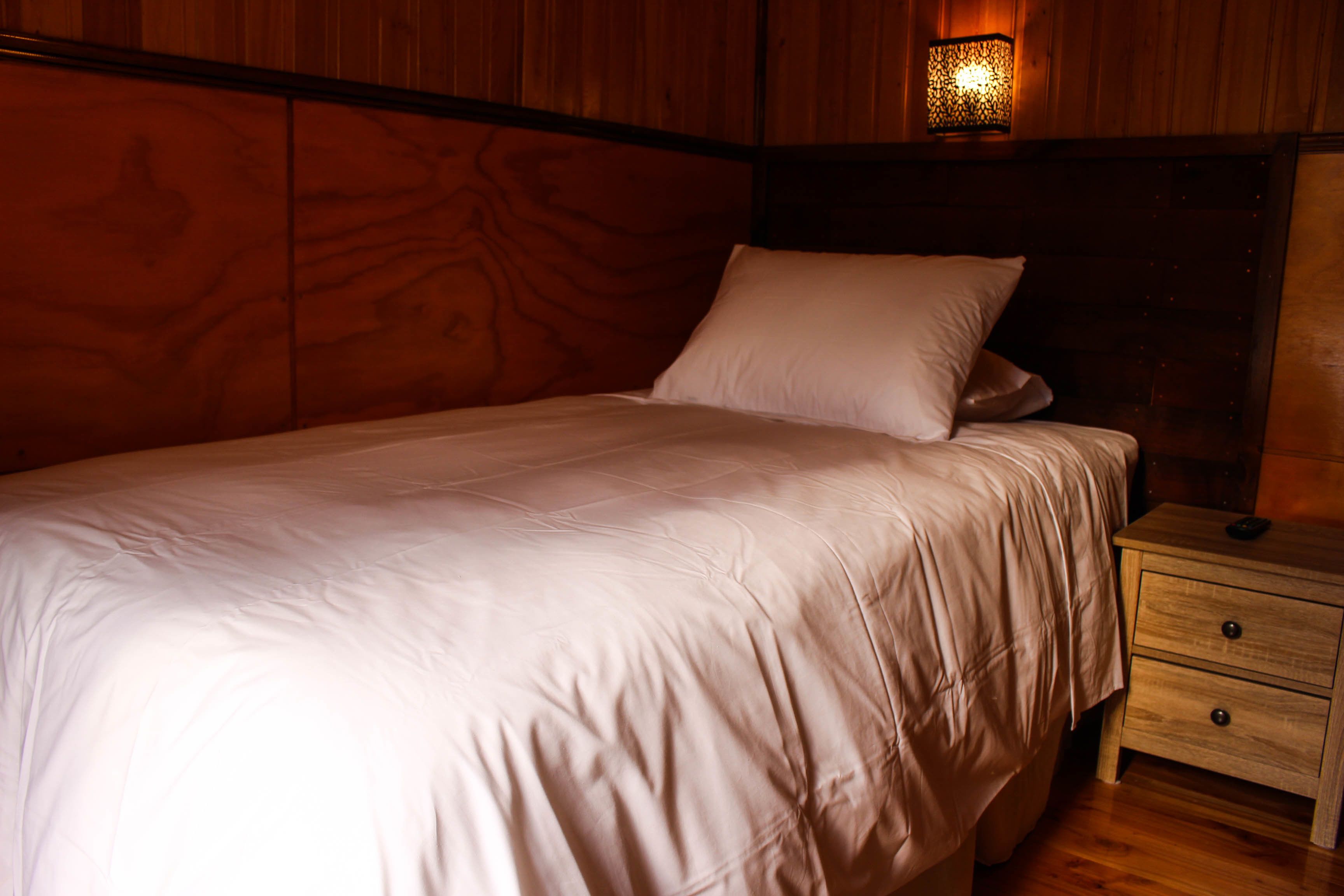 A neatly made bed with a wooden headboard and a bedside table with drawers.