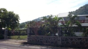 A gated entrance with a stone wall and metal fence, leading to a building with a red roof and white walls.