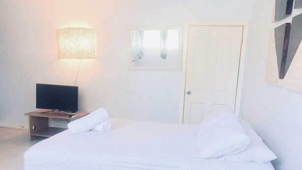 A bedroom with a bed, a television on a stand, a door, and a wall-mounted light fixture.