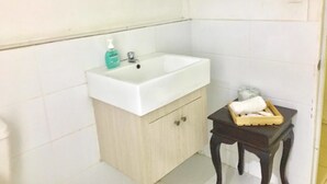 A bathroom with a white sink, a wooden cabinet, and a small table with toiletries.