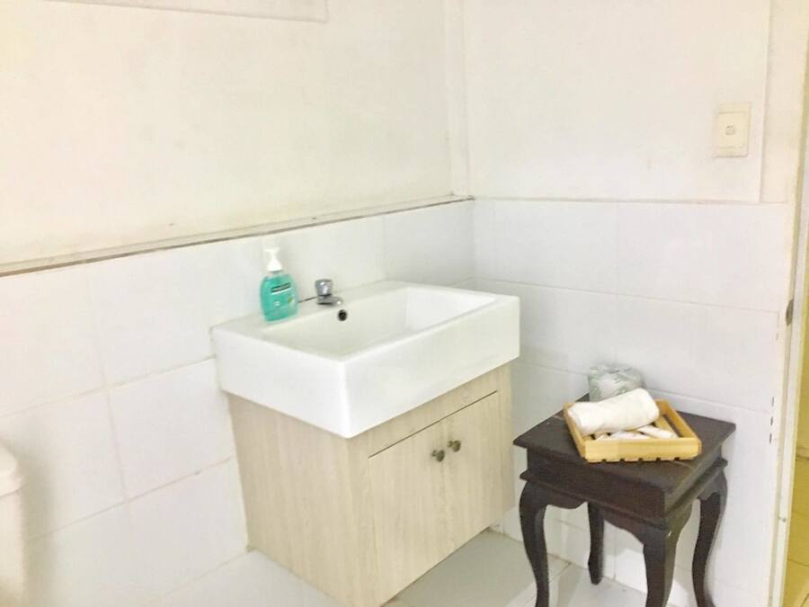 Un baño con un lavamanos blanco, un mueble de madera y una mesita con artículos de aseo.