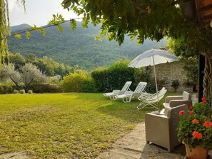 Ein Garten mit einer Steinmauer, weißen Liegestühlen und einer Pergola mit einem gestreiften Sonnenschirm.
