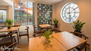 A modern dining area with wooden tables and chairs, potted plants, and a large wall clock. - Mojzo Inn Boutique (Nha Trang)