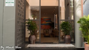 The entrance of a hotel with a modern design, featuring a glass facade, a signboard, and potted plants. - Mojzo Inn Boutique (Nha Trang)
