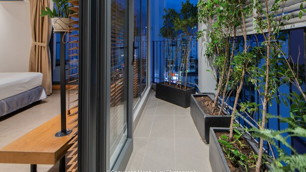 A modern balcony with a bed, potted plants, and a view of the cityscape at dusk. - Mojzo Inn Boutique (Nha Trang)