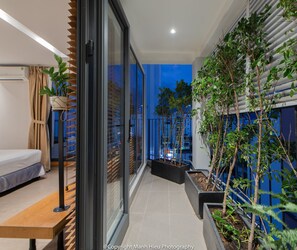 Ein moderner Balkon mit Bett, Topfpflanzen und Blick auf die Stadt bei Dämmerung.
