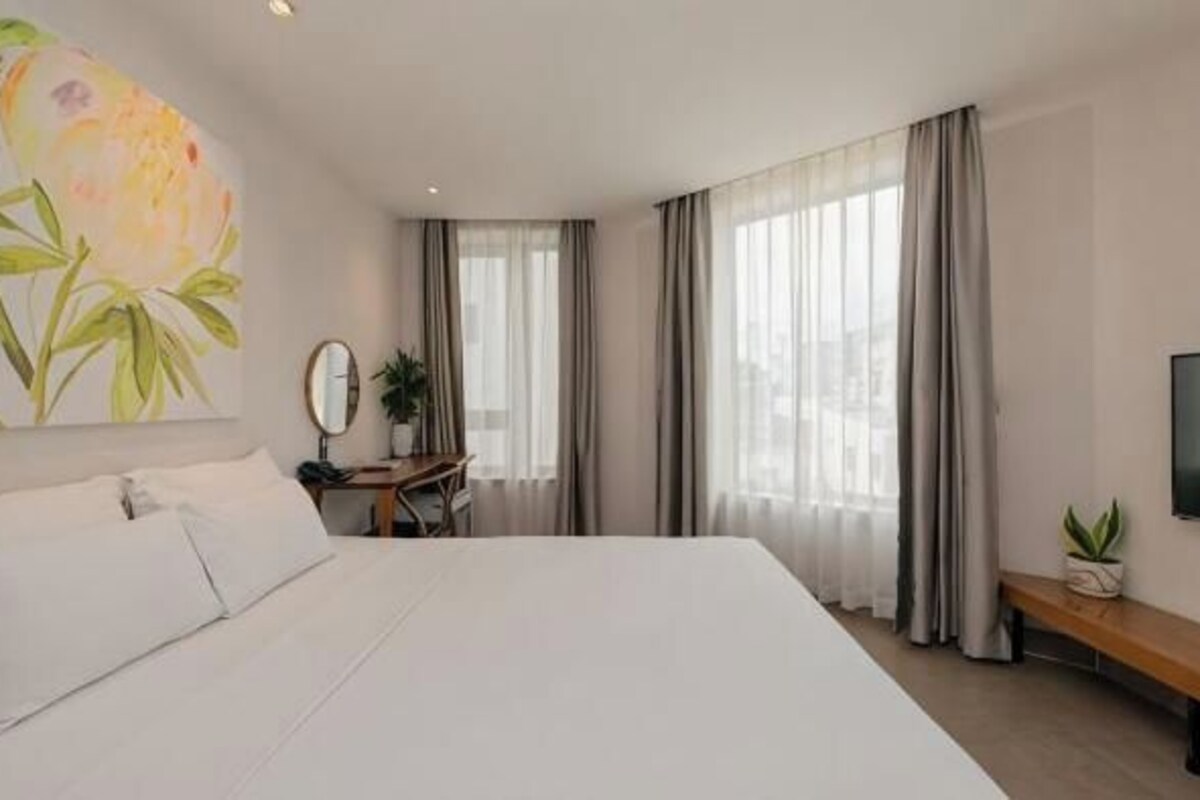 A hotel room with a large bed, a desk with a chair, a TV, and a window with curtains.