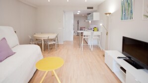 Una sala de estar moderna con un sofá, una mesita auxiliar amarilla, un televisor y una zona de comedor con una mesa y sillas.