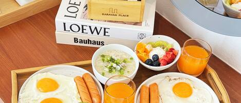 A breakfast tray with eggs, sausages, soup, and fruit on a wooden table.