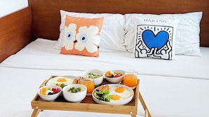 Een opgemaakt bed met een houten hoofdbord, twee decoratieve kussens en een dienblad met ontbijtartikelen.