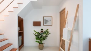 Een hal met een houten trap, een potplant, een ingelijst foto en een wit draagbaar schilderblok tegen de muur.