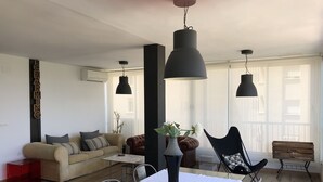 Uma sala de estar moderna com uma mesa de centro de vidro, um sofá, uma poltrona de couro e uma mesa de jantar com toalha branca.