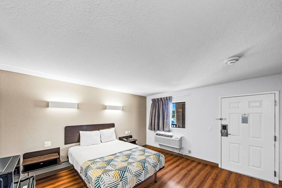 A hotel room with a bed, bedside table, lamp, and a window with curtains.