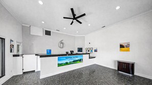 Un espace d’accueil moderne avec un ventilateur de plafond noir, un comptoir doté d’un écran numérique et une grande affiche publicitaire pour un service.