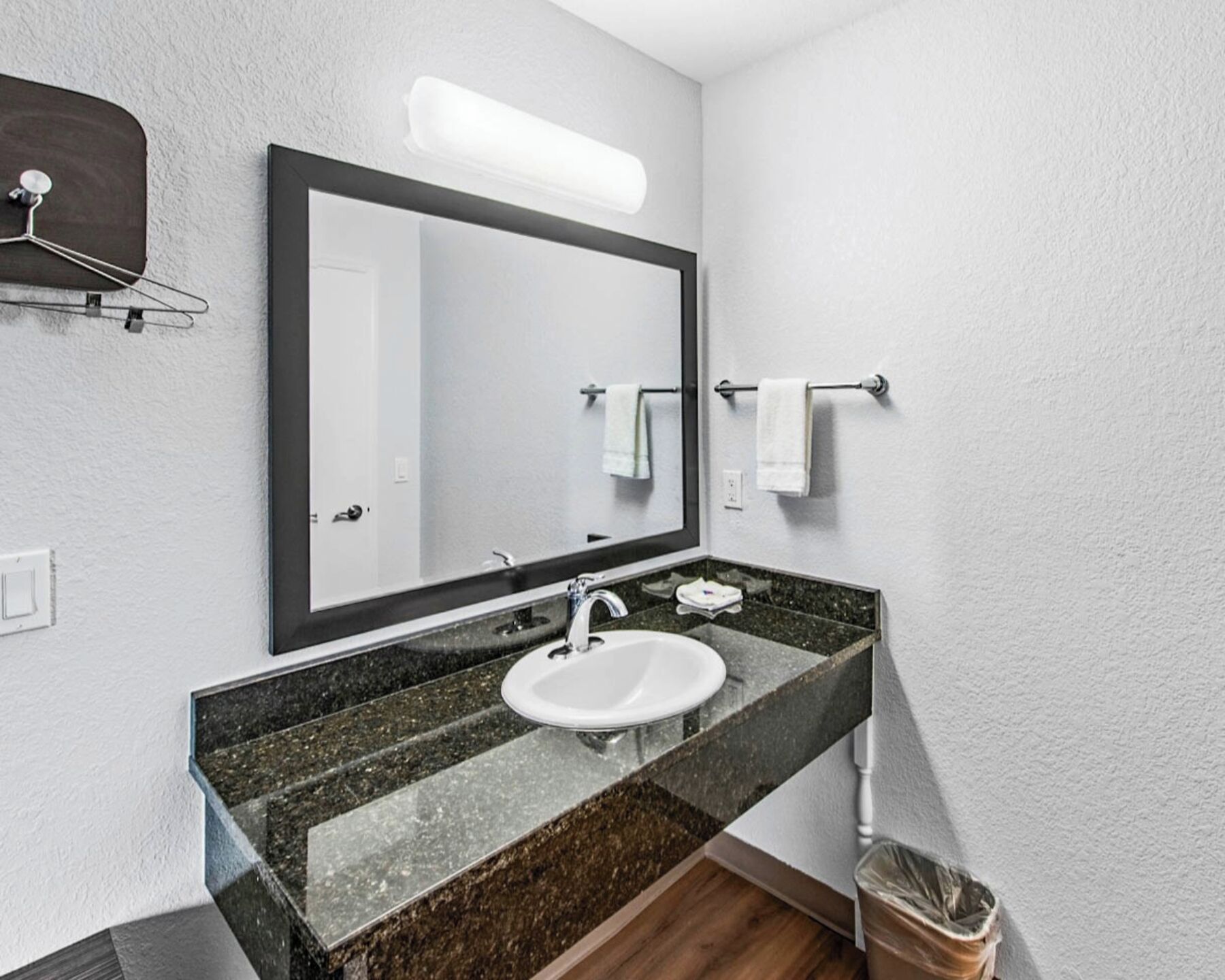 A bathroom with a white sink, dark granite countertop, a large mirror, and a towel rack.