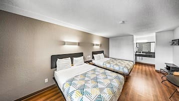 A hotel room with two beds, a small kitchenette, and a bathroom.