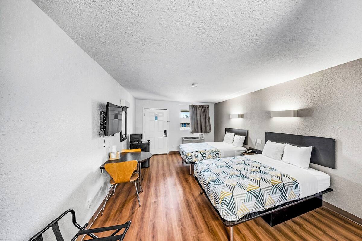 A hotel room with two beds, a desk, and a chair.