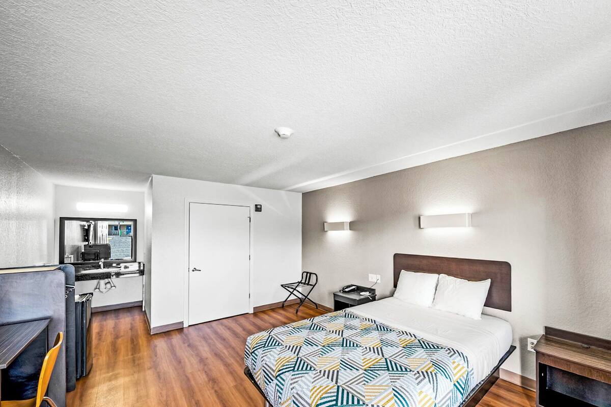 A hotel room with a bed, a desk, a chair, a nightstand, and a small table.