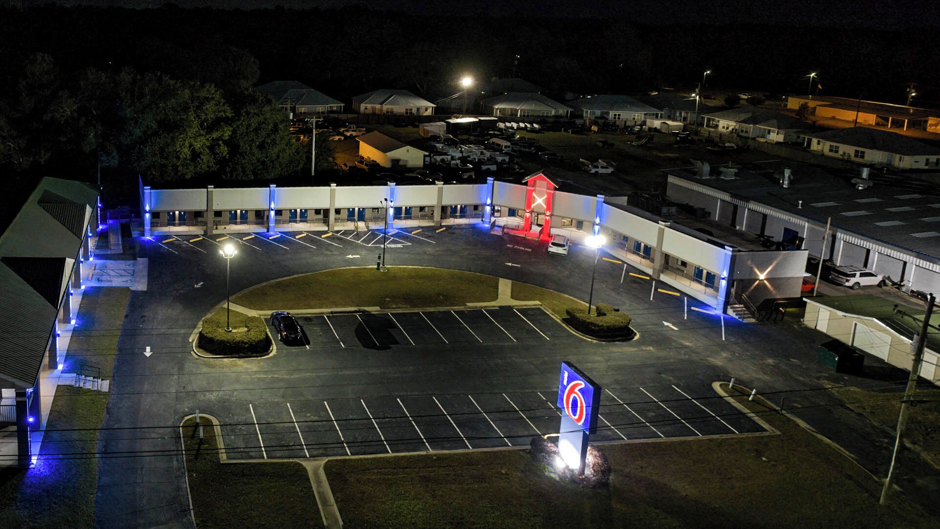 An aerial view of a parking lot with multiple parking spaces, a central landscaped area, and a building with a distinctive red and blue sign.