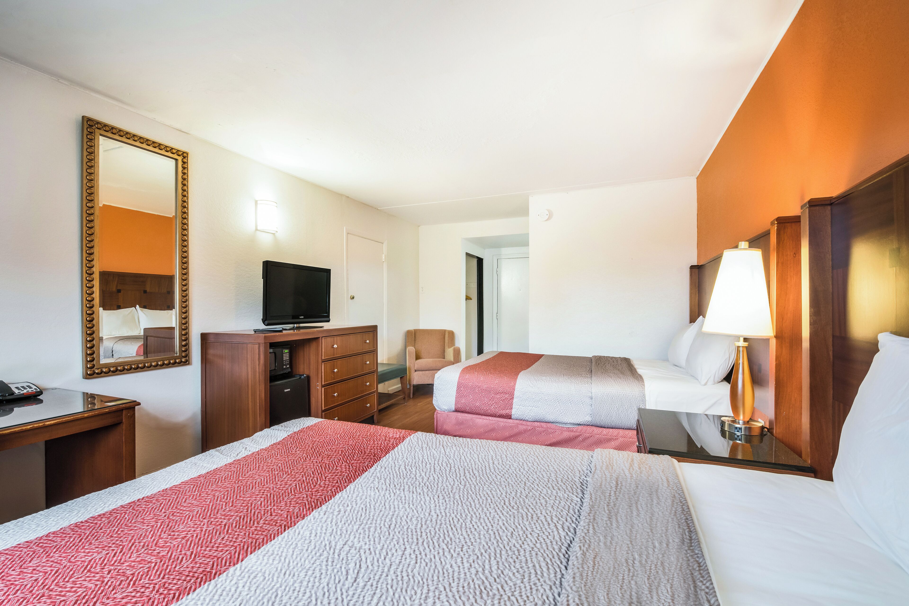 A hotel room with two beds, a desk, a television, a dresser, and a lamp.