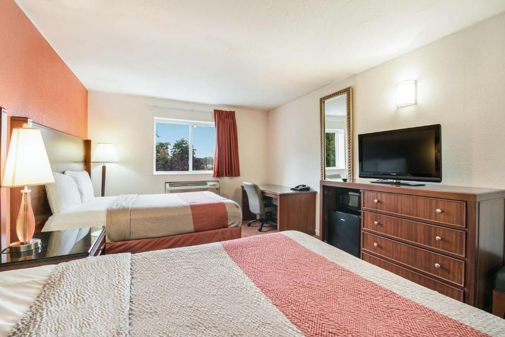 A hotel room with two beds, a desk, a television, and a dresser.